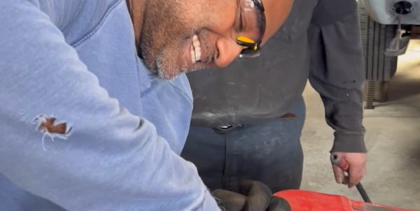 Autoseum student using a drill-mounted wire brush along the edge of a removed red car door
