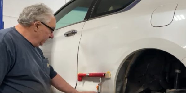 Technician working on a white car’s rear quarter panel with red pulling equipment attached to glued wood blocks
