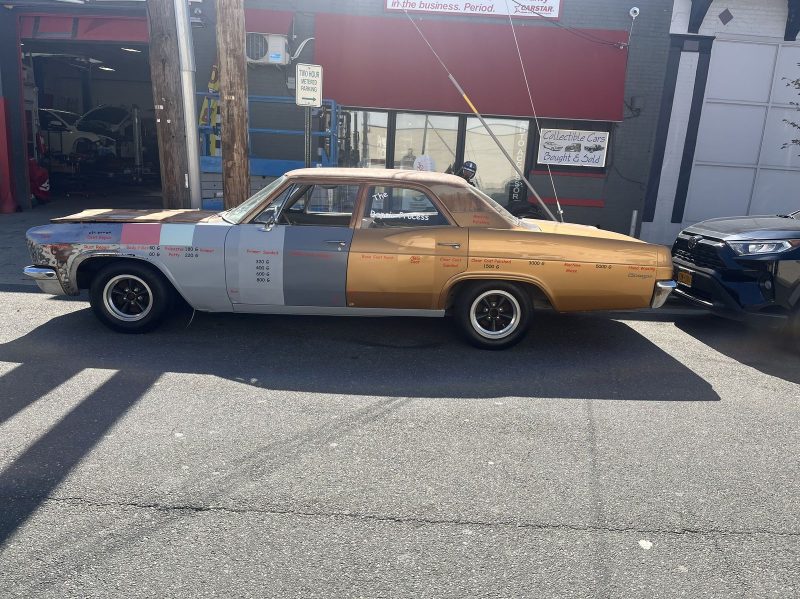 Classic sedan in primer parked in front of the shop